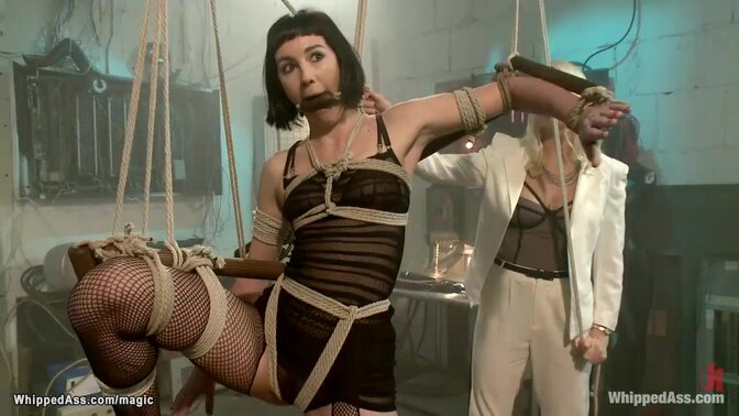 Lesbian blonde dom lady Lorelei Lee whipping gagged brunette slave Coral Aorta in lingerie with bent leg in the air then fucking her with strap on